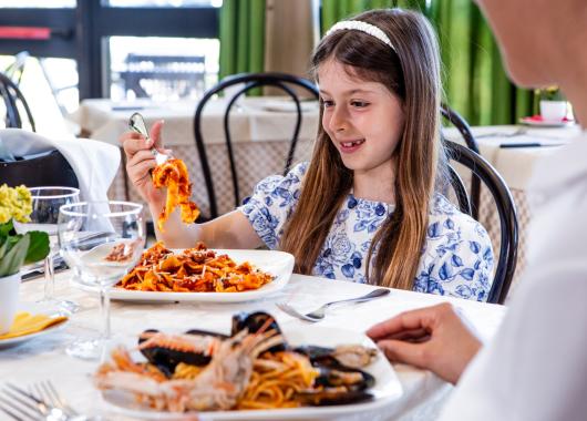 Girl eating pasta in a restaurant, smiling and happy.