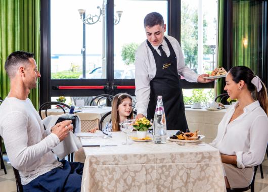 Family dining at a restaurant, waiter serving delicious dishes.