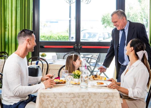 Family dining at restaurant, smiling waiter.