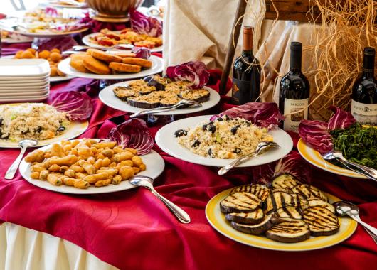 Buffet with Italian dishes and wine bottles on a red tablecloth.