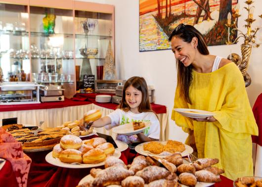 Mother and daughter choose pastries at a colorful buffet.