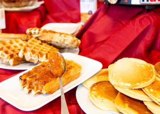 Breakfast with waffles, pancakes, and jam on a red tablecloth.