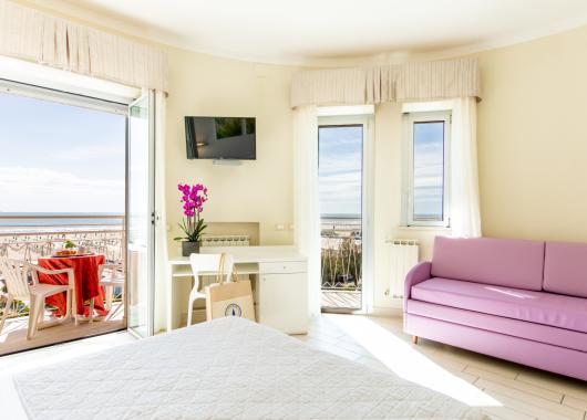 Bright room with sea view, purple sofa, and balcony.