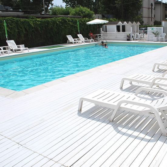 Piscina all'aperto con lettini bianchi e ombrelloni verdi.