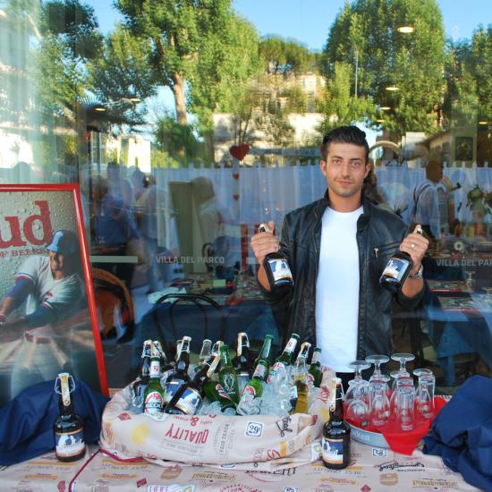 Uomo con giacca di pelle tiene bottiglie di birra davanti a un negozio.