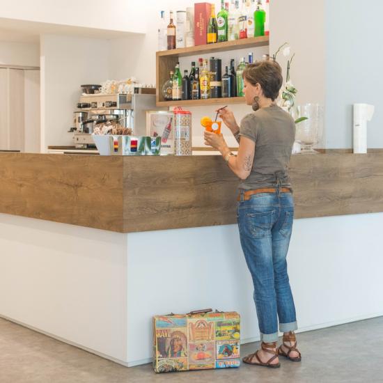 Donna al bar con drink, valigia vintage accanto.