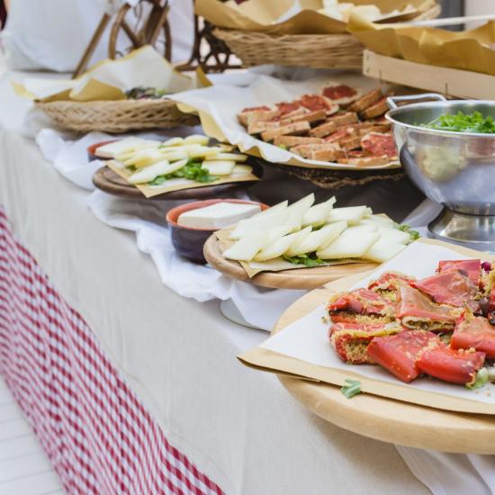 Buffet con formaggi, verdure e pane su tavolo con tovaglia a quadretti.