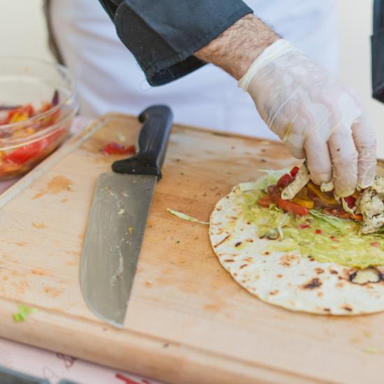 Preparazione di un burrito su un tagliere con guanti.