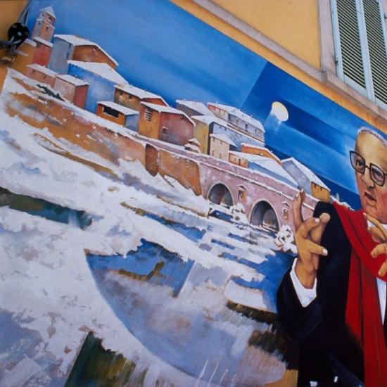 Murale colorato su edificio con paesaggio e figura con sciarpa rossa.