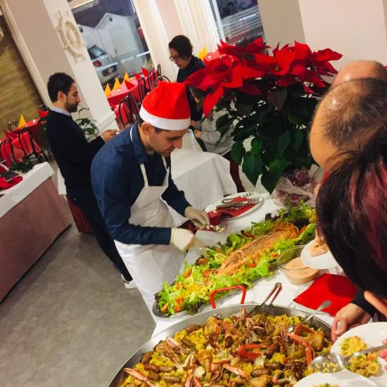 Buffet natalizio con grande piatto di paella e decorazioni festive.