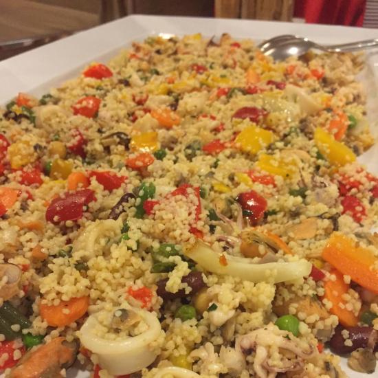 Couscous con frutti di mare e verdure colorate su piatto bianco.