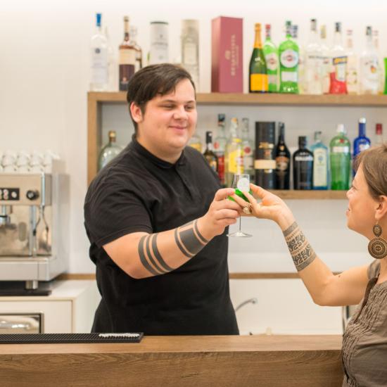 Un brindisi al bar tra due persone sorridenti.