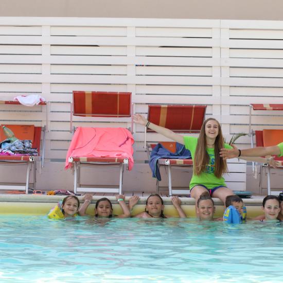 Gruppo di bambini in piscina con due istruttori sorridenti.