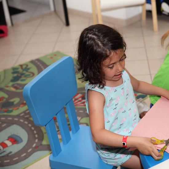 Bambina che ritaglia carta rosa con le forbici.