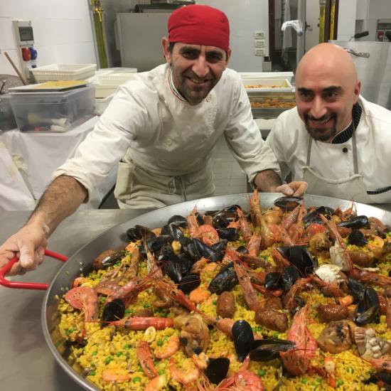 Due chef con una grande paella ai frutti di mare in cucina.