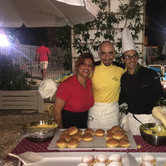 Tre cuochi sorridenti con dolci alla crema in una festa all'aperto.