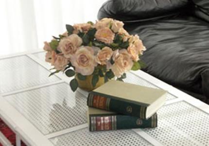 Coffee table with pink flowers and two books, near a black sofa.