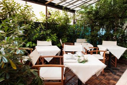 Outdoor garden with set tables and chairs, surrounded by green plants.