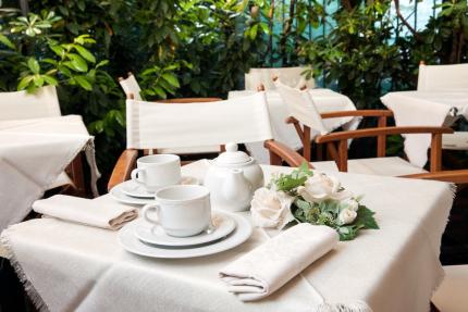 Elegant table with tea cups and white flowers, surrounded by green plants.