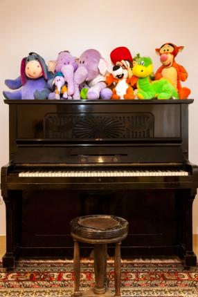 Colorful plush toys on a black piano with stool.