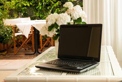 Laptop on glass table with white flowers, outdoors.