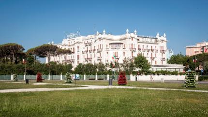 Elegant hotel with garden, Italian flags, clear sky.