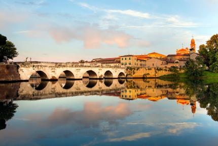 Ancient bridge reflected in water at sunset, framed by a clear sky.