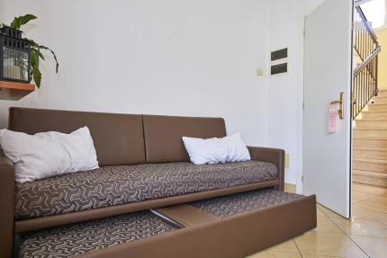 Brown sofa bed with white pillows near stairs.