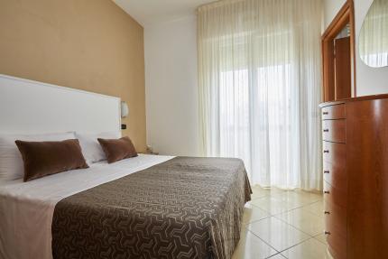 Modern bedroom with double bed and sheer curtains.