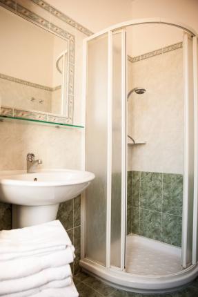 Bathroom with corner shower, sink, and mirror, green and white tiles.