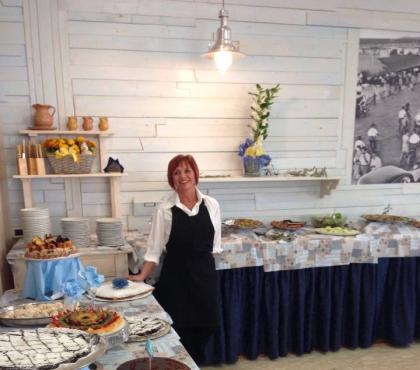 Buffet di dolci con torte varie, donna sorridente accanto al tavolo.