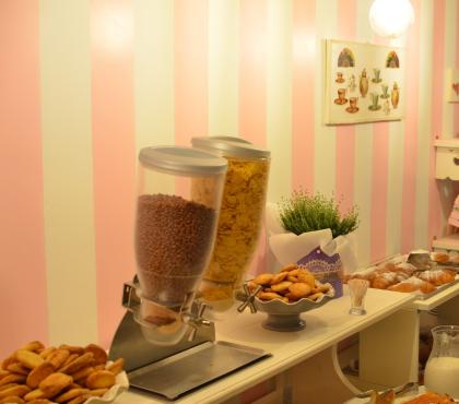 Buffet con cereali, dolci e latte in una sala colazione accogliente.