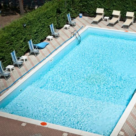 Piscina all'aperto con sdraio e ombrelloni su pavimentazione in mattoni.