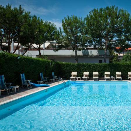 Piscina all'aperto con lettini e alberi intorno.