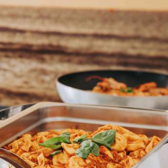 Tortellini al ragù in un vassoio di metallo, decorati con basilico.