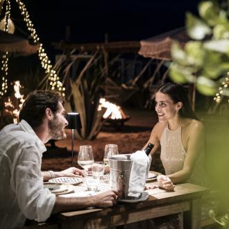 Cena romantica sulla spiaggia con luci soffuse e vino.