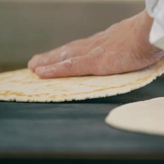 Mano che prepara piadine su una piastra calda.