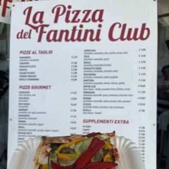 Pizza al taglio con verdure davanti al menu del Fantini Club.