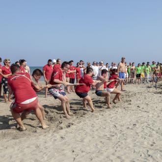 Gara di tiro alla fune sulla spiaggia tra squadre in rosso e verde.