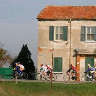 Ciclisti pedalano accanto a una casa rustica in campagna.