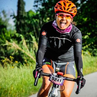 Ciclista sorridente con casco arancione su strada alberata.