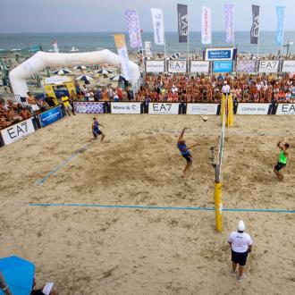 Partita di beach volley su spiaggia affollata.