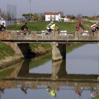 Ciclisti attraversano un ponte sopra un canale in campagna.