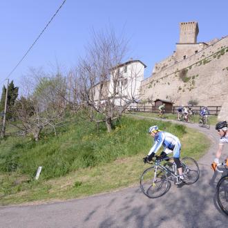 Ciclisti pedalano vicino a un castello medievale in una giornata soleggiata.