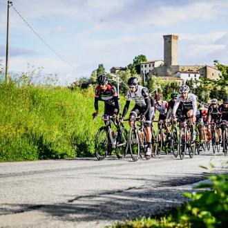 Ciclisti in gara su strada di campagna con castello sullo sfondo.