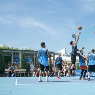 Partita di basket all'aperto con giocatori in azione sotto il sole.