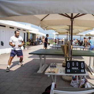 Partita di ping pong all'aperto in spiaggia sotto ombrelloni.