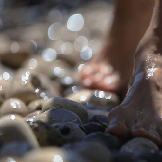 Piedi nudi camminano su sassi bagnati, riflessi di luce.