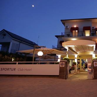 Hotel illuminato di sera con ingresso accogliente e ombrelloni.