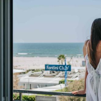 Donna in abito bianco guarda il mare da un balcone.